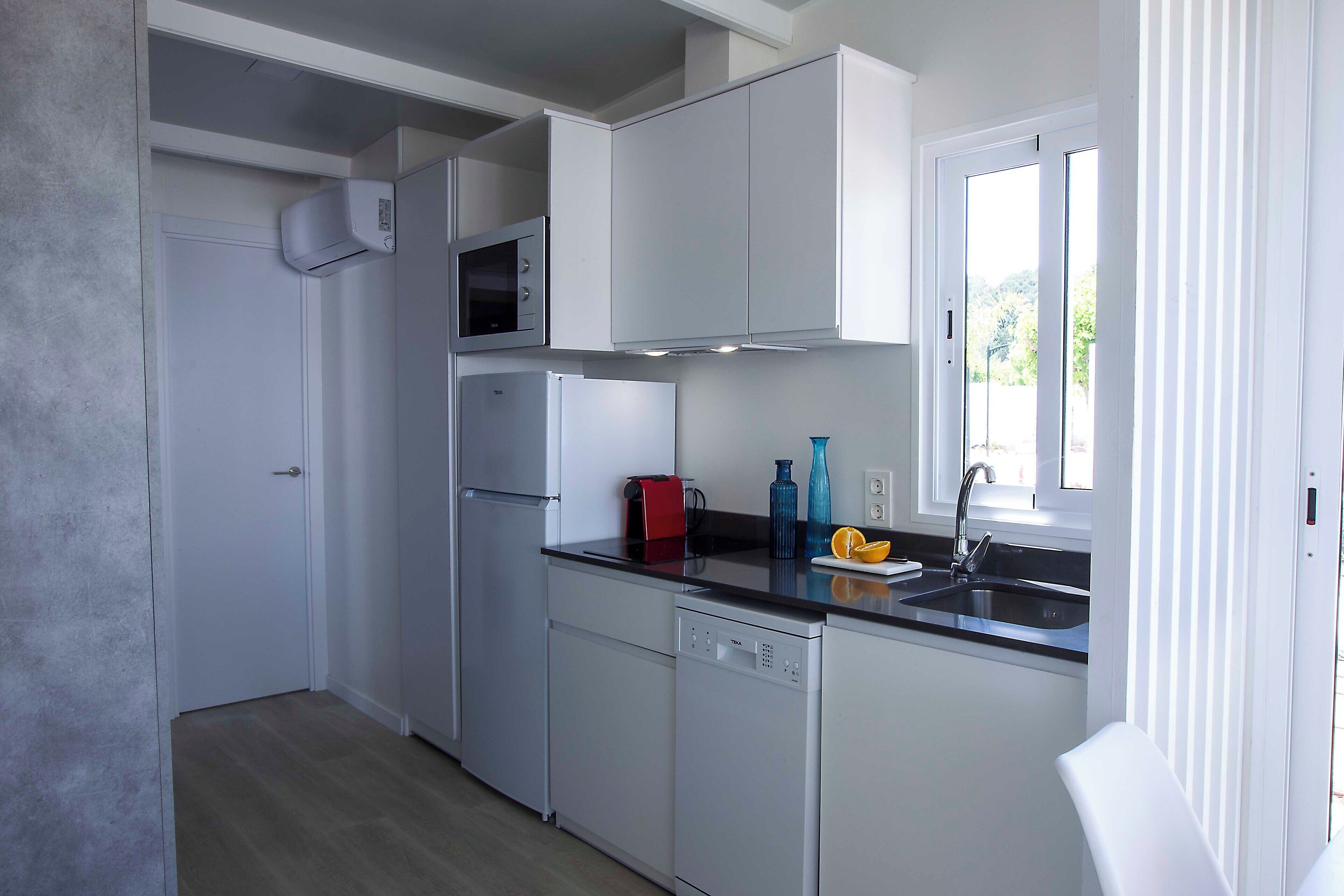 A modern kitchen with white cabinets, a built-in microwave, a dishwasher, and a window providing natural light.
