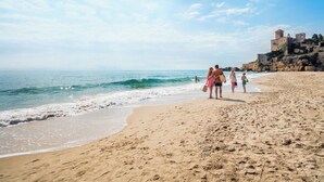 A sandy beach with a clear sky, waves, and a historic building in the background. - Tamarit Beach Resort (Tarragona)