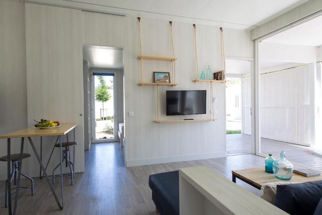 A modern living room with a TV mounted on a wall, a wooden table with chairs, and a bench.