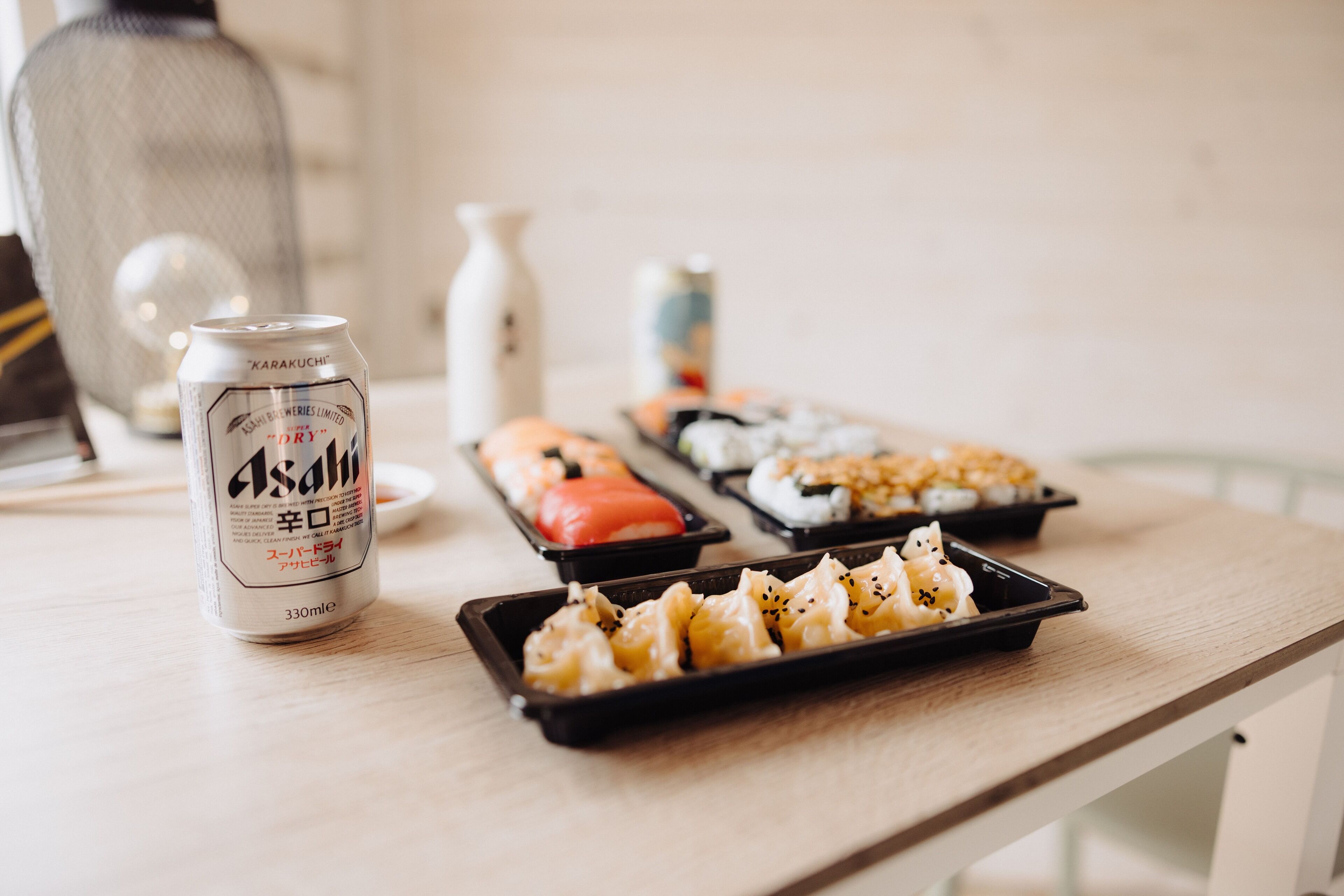 Una mesa con una lata de cerveza Asahi, sushi y una pieza decorativa de cerámica.