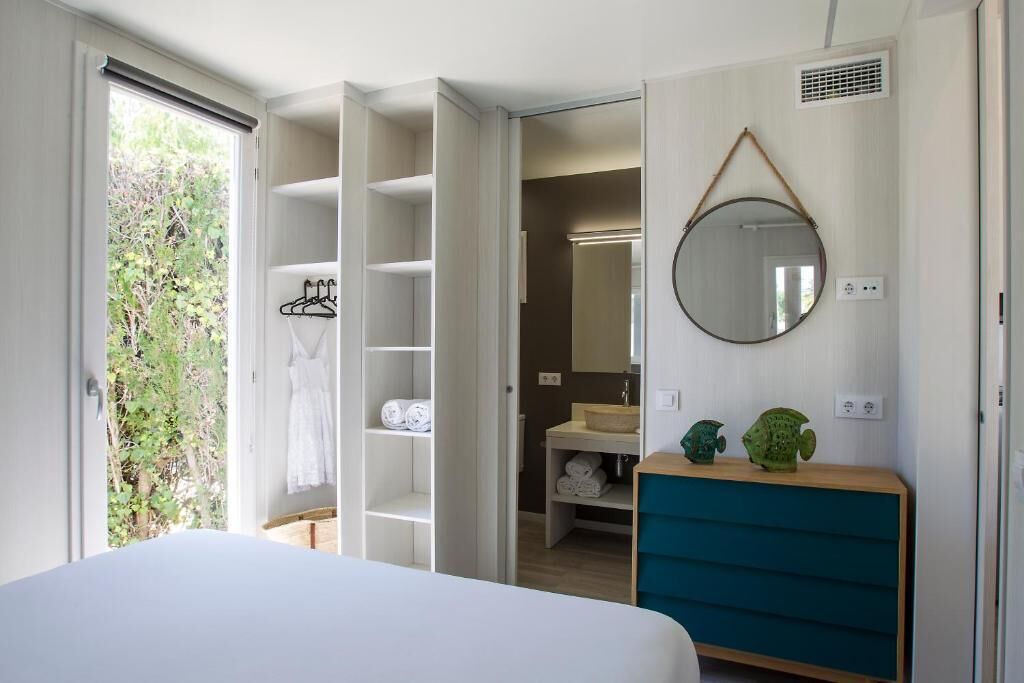 Una camera da letto con un letto, un armadio, uno specchio e un bagno con lavandino e porta asciugamani.