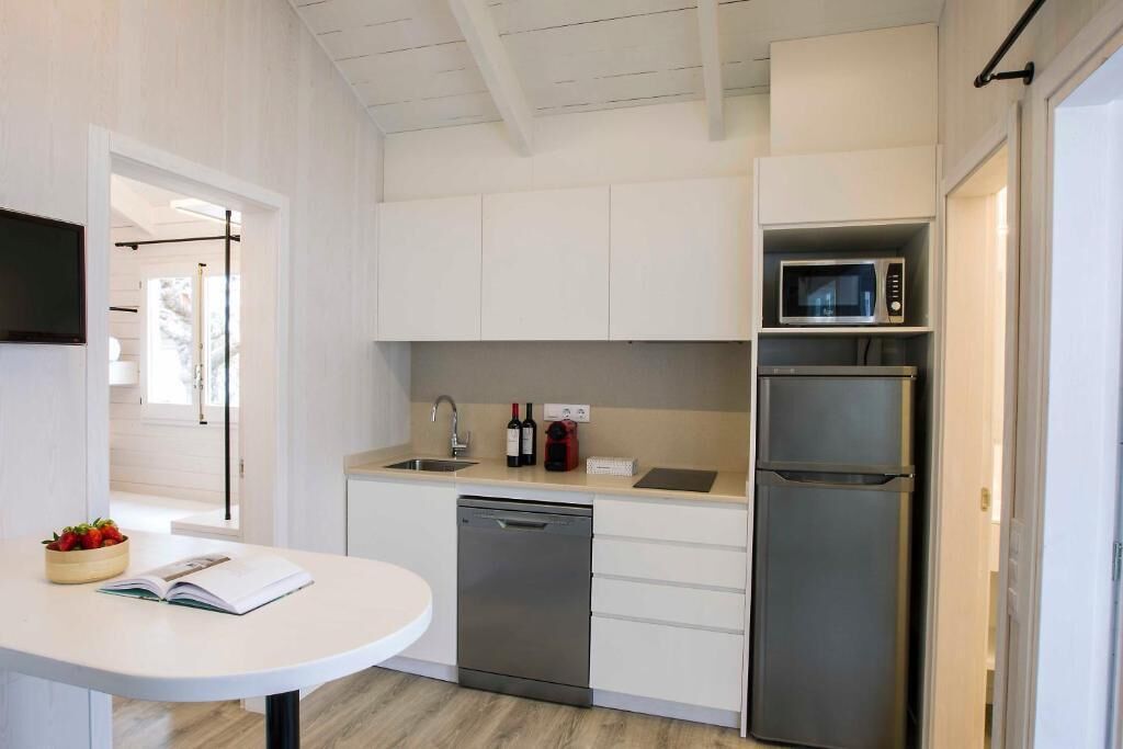 Una cocina compacta con gabinetes blancos, microondas integrado, refrigerador de acero inoxidable y lavavajillas.