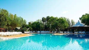 A clear blue pool surrounded by lounge chairs and palm trees. - Tamarit Beach Resort (Tarragona)