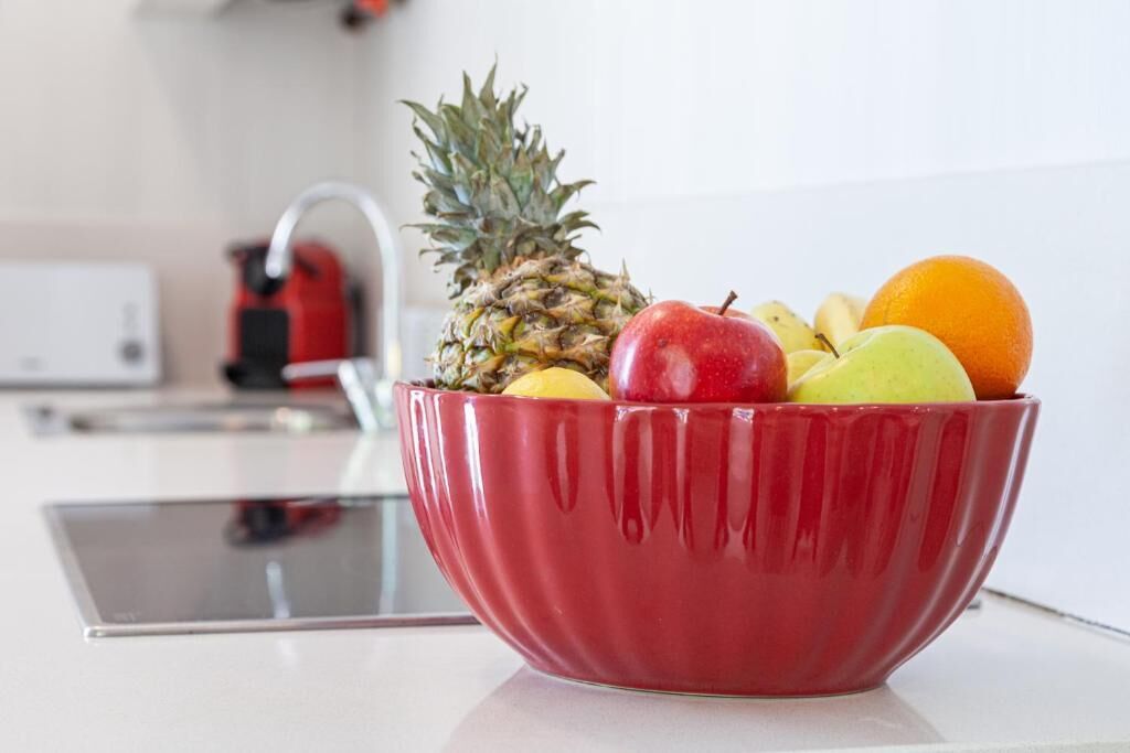 Eine rote Schüssel mit Ananas, Apfel, Banane und Orange auf einer Küchenarbeitsplatte.