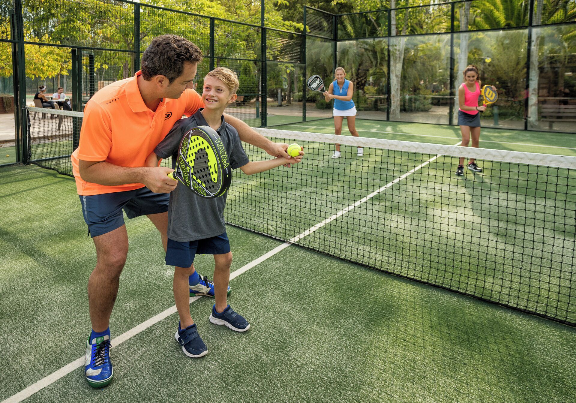 Una cancha de tenis con jugadores y un entrenador.