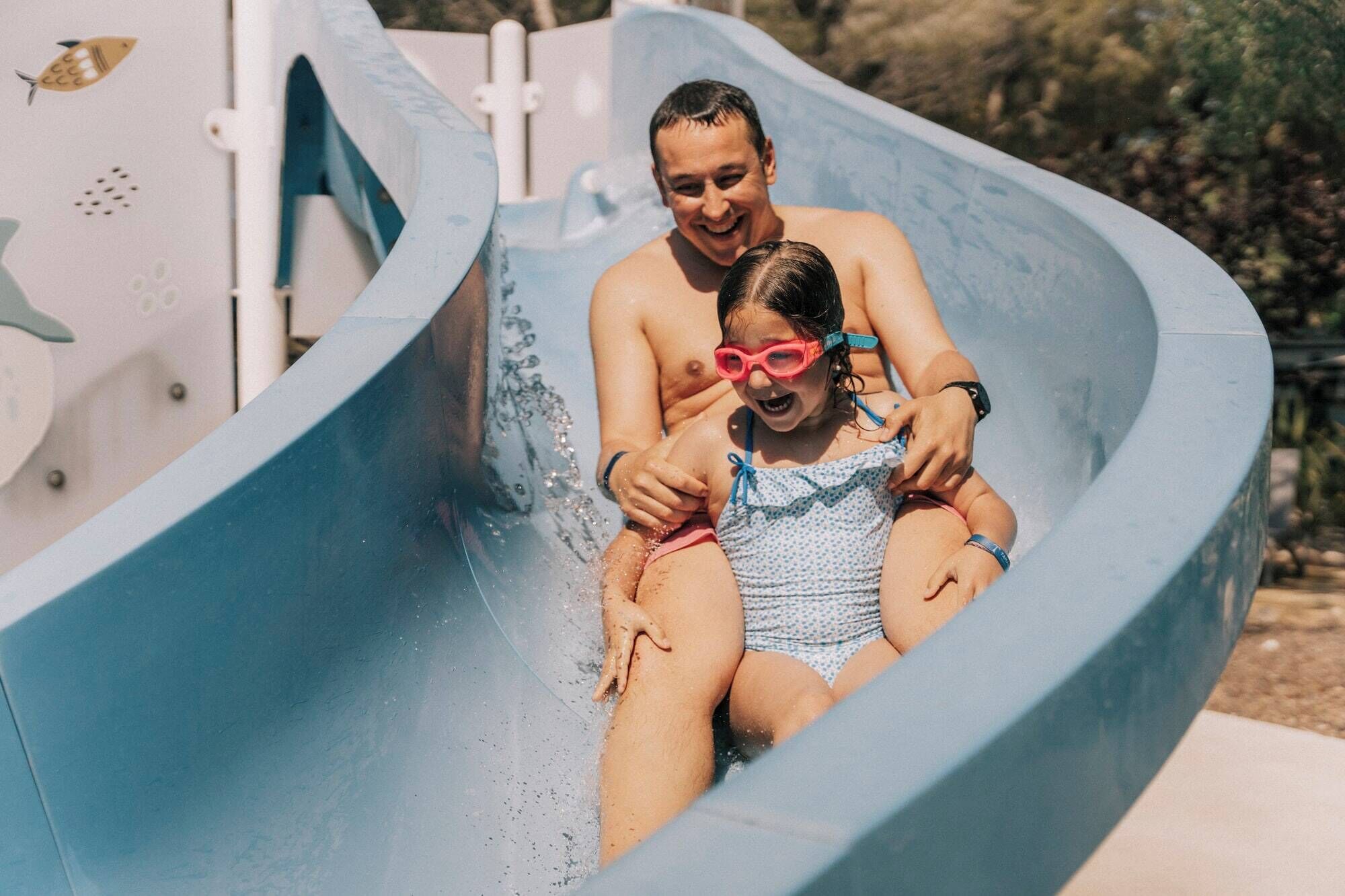 A water slide with a person and a child at the top, water splashing around.