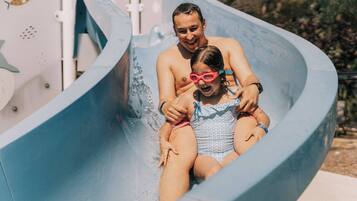 A water slide with a person and a child at the top, water splashing around.