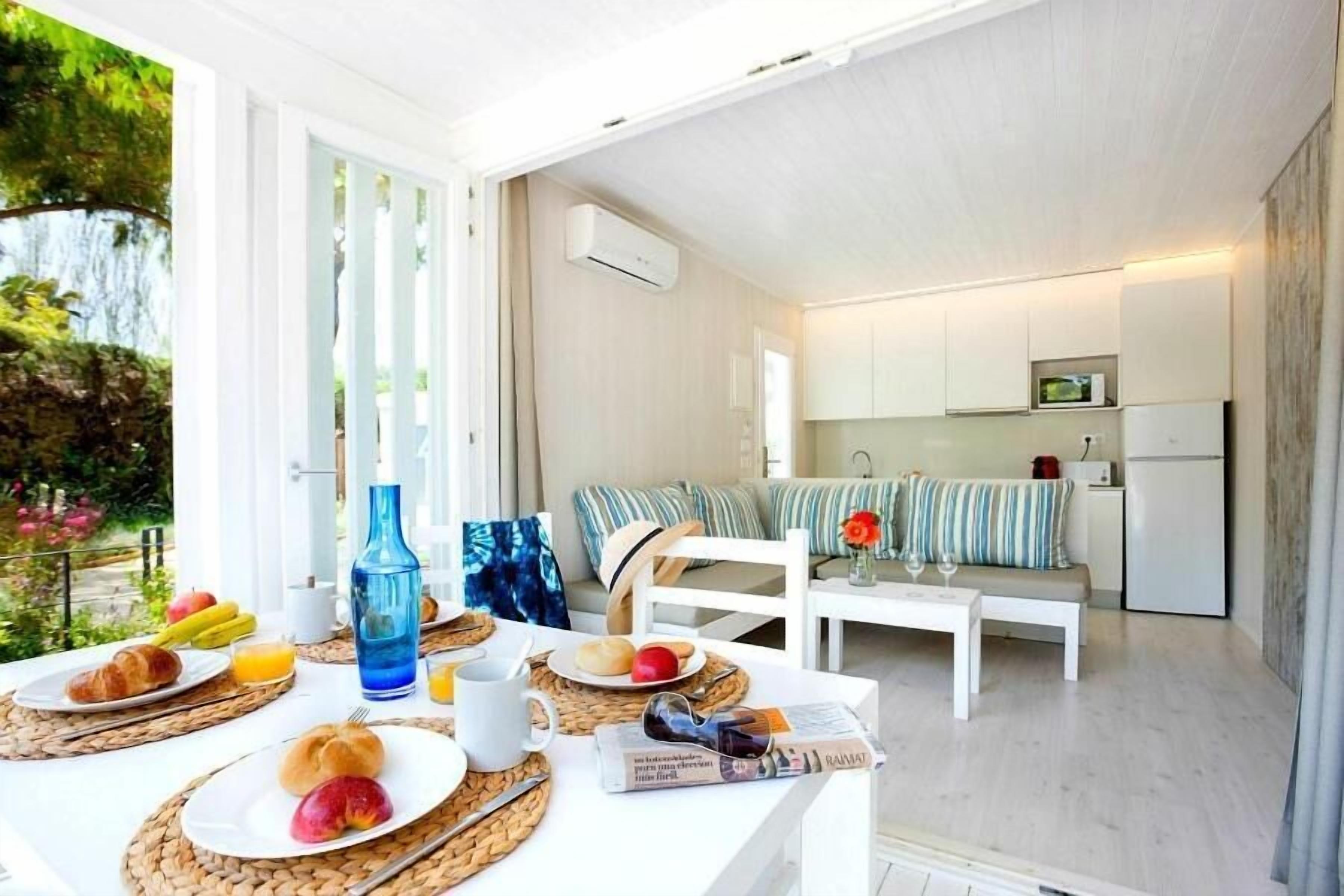 Una cocina moderna con armarios blancos, un comedor con una mesa blanca dispuesta para el desayuno y vistas al exterior.