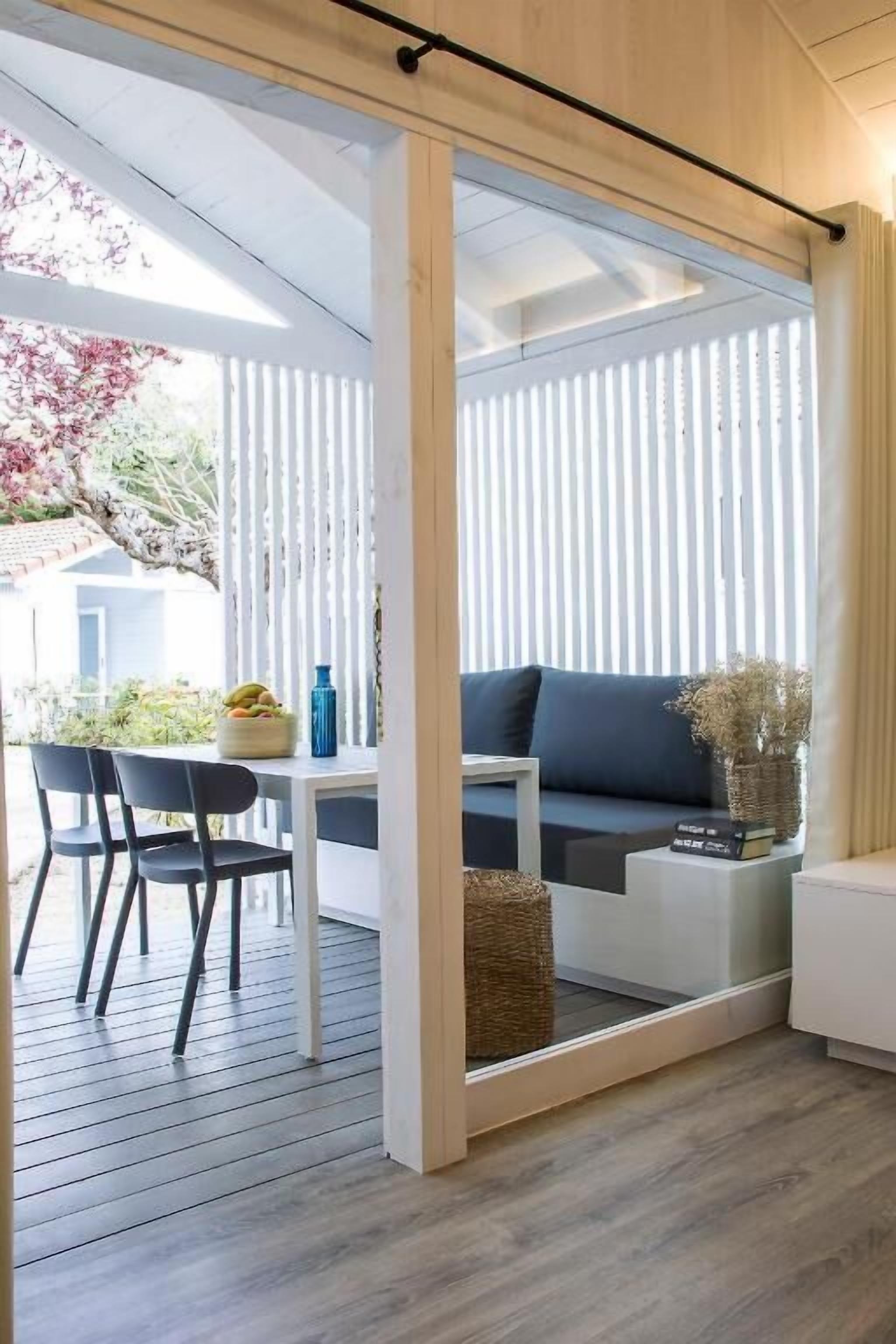 Un espacio moderno para la vida con un sofá, una mesa de comedor con sillas y un amplio ventanal con persianas verticales.