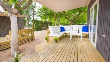 A wooden deck with a white sofa and blue cushions, surrounded by trees and a covered area.