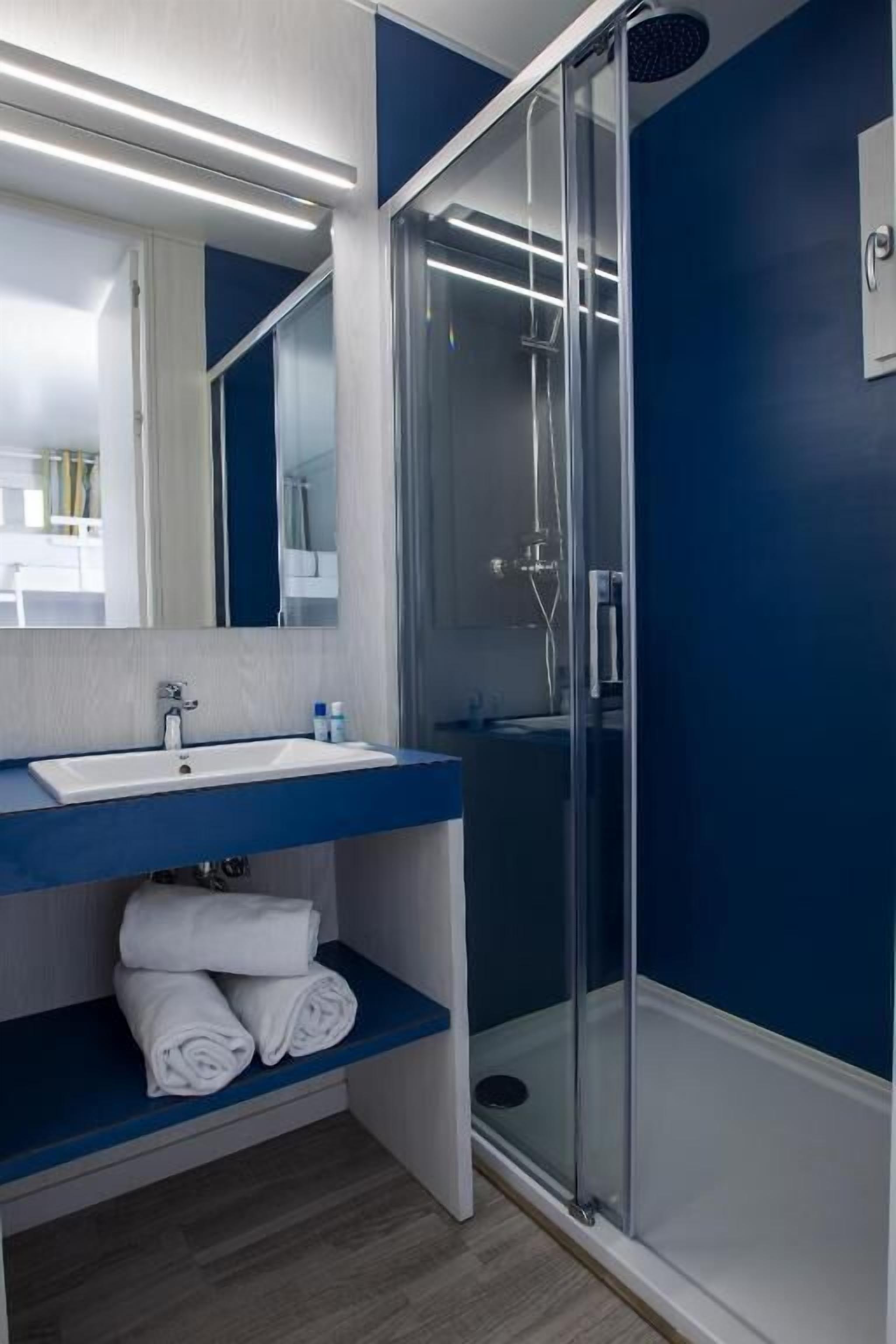 Un baño con ducha de mampara de vidrio, un lavamanos blanco y un espejo encima.
