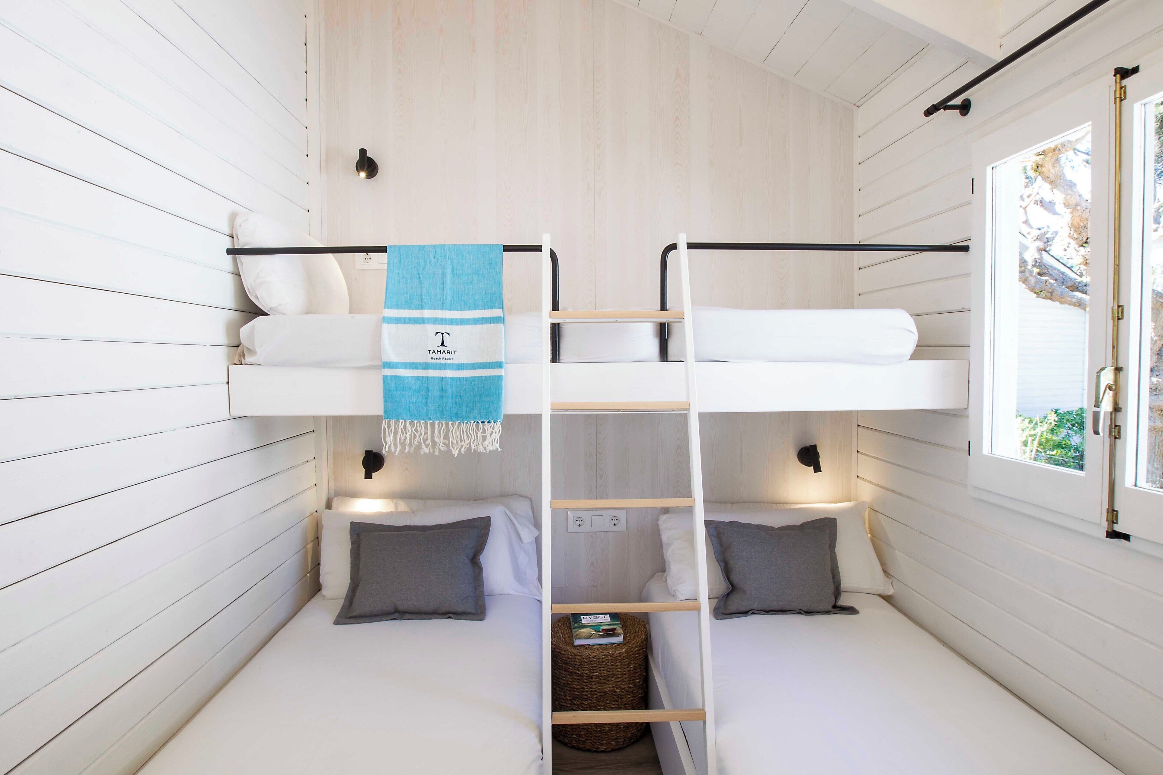 Une chambre avec un lit superposé, une échelle, une fenêtre avec vue et une serviette ornée d’un logo.