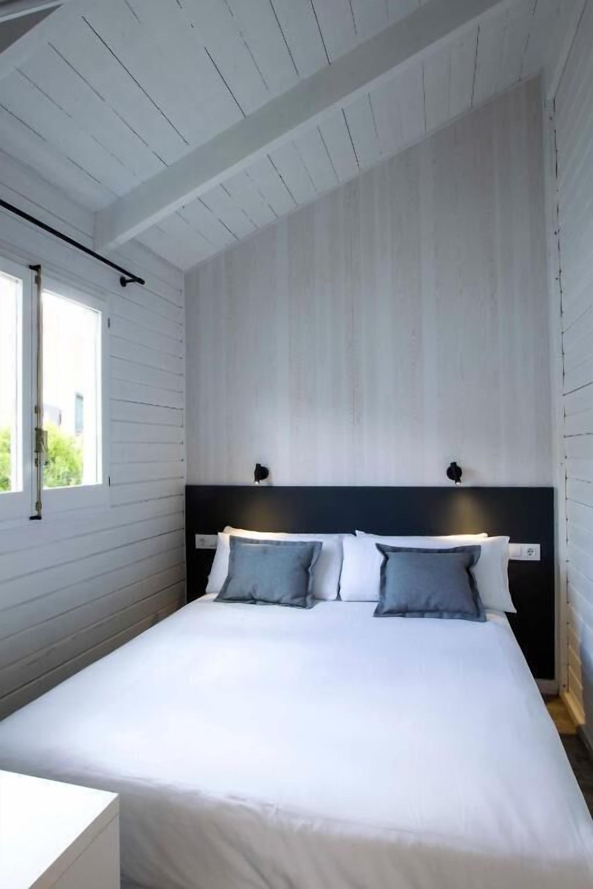 Un dormitorio moderno con una cama blanca, un cabecero oscuro y una ventana con vistas a zonas verdes.