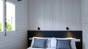 Un dormitorio moderno con una cama blanca, un cabecero oscuro y una ventana con vistas a zonas verdes.