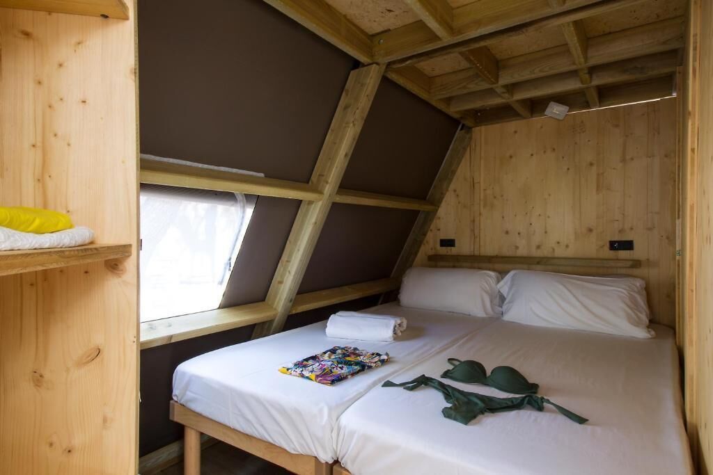 Un dormitorio pequeño de madera estilo ático con una cama individual, una ventana y una repisa con un objeto amarillo.