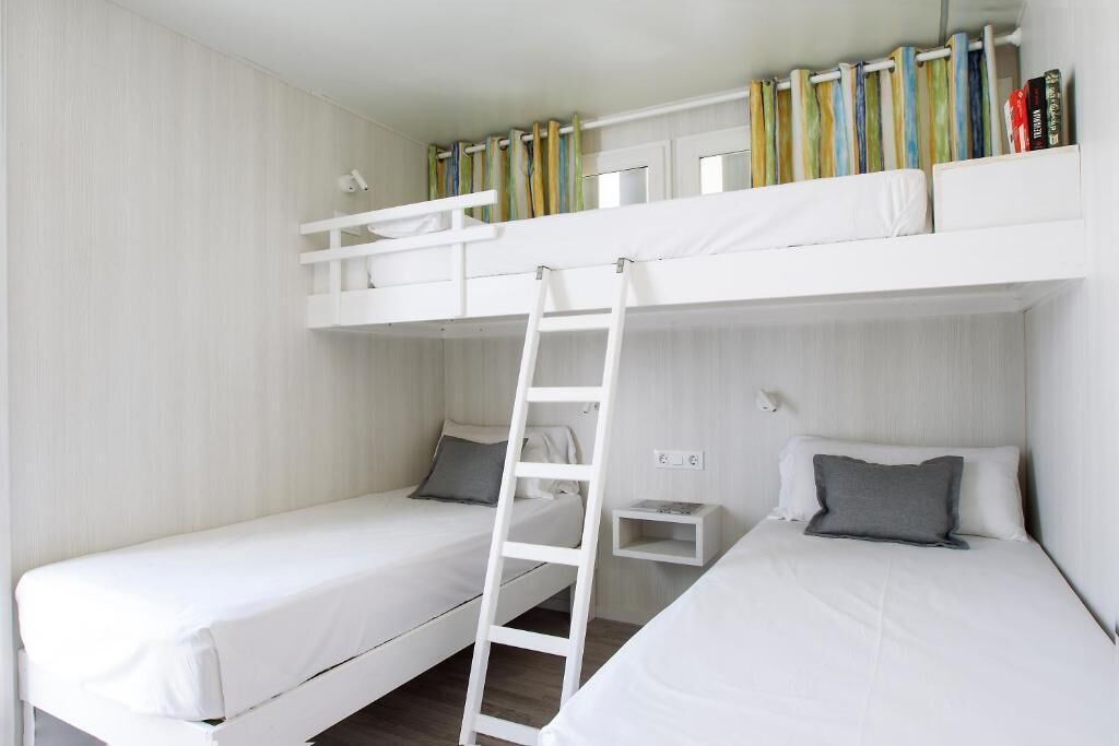 A bunk bed room with a ladder, a small shelf, and a window with curtains.
