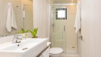 Un bagno moderno con lavandino, specchio e WC bianchi, box doccia in vetro e una pianta in vaso sul mobile.