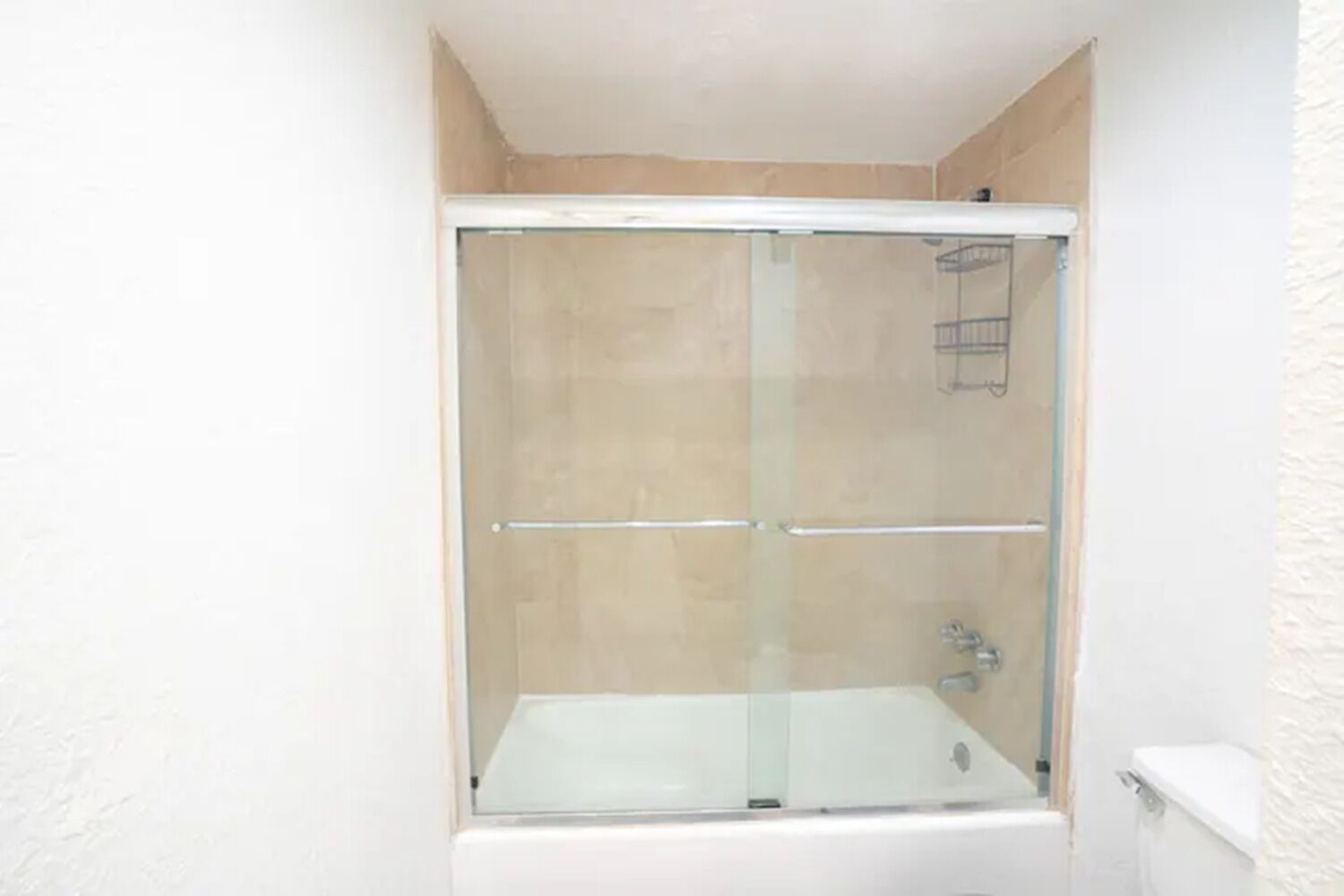 Un petit espace douche fermé, doté d’une porte en verre, d’une baignoire blanche et d’un porte-serviettes.