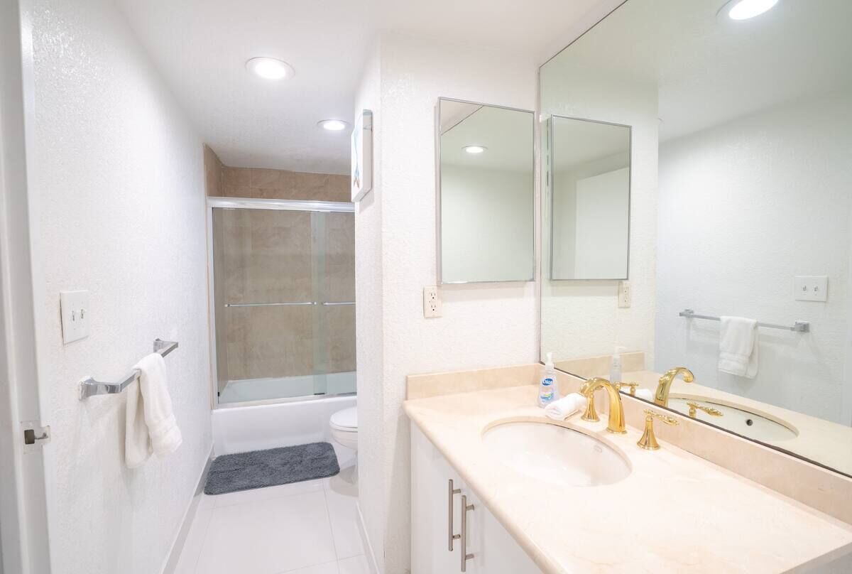 A bathroom with a bathtub, a shower, a sink with gold faucets, and a large mirror.