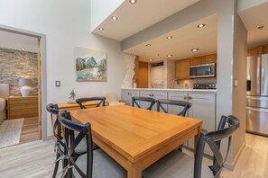 Cozinha moderna com ilha central, eletrodomésticos embutidos e área de jantar com mesa e cadeiras de madeira.