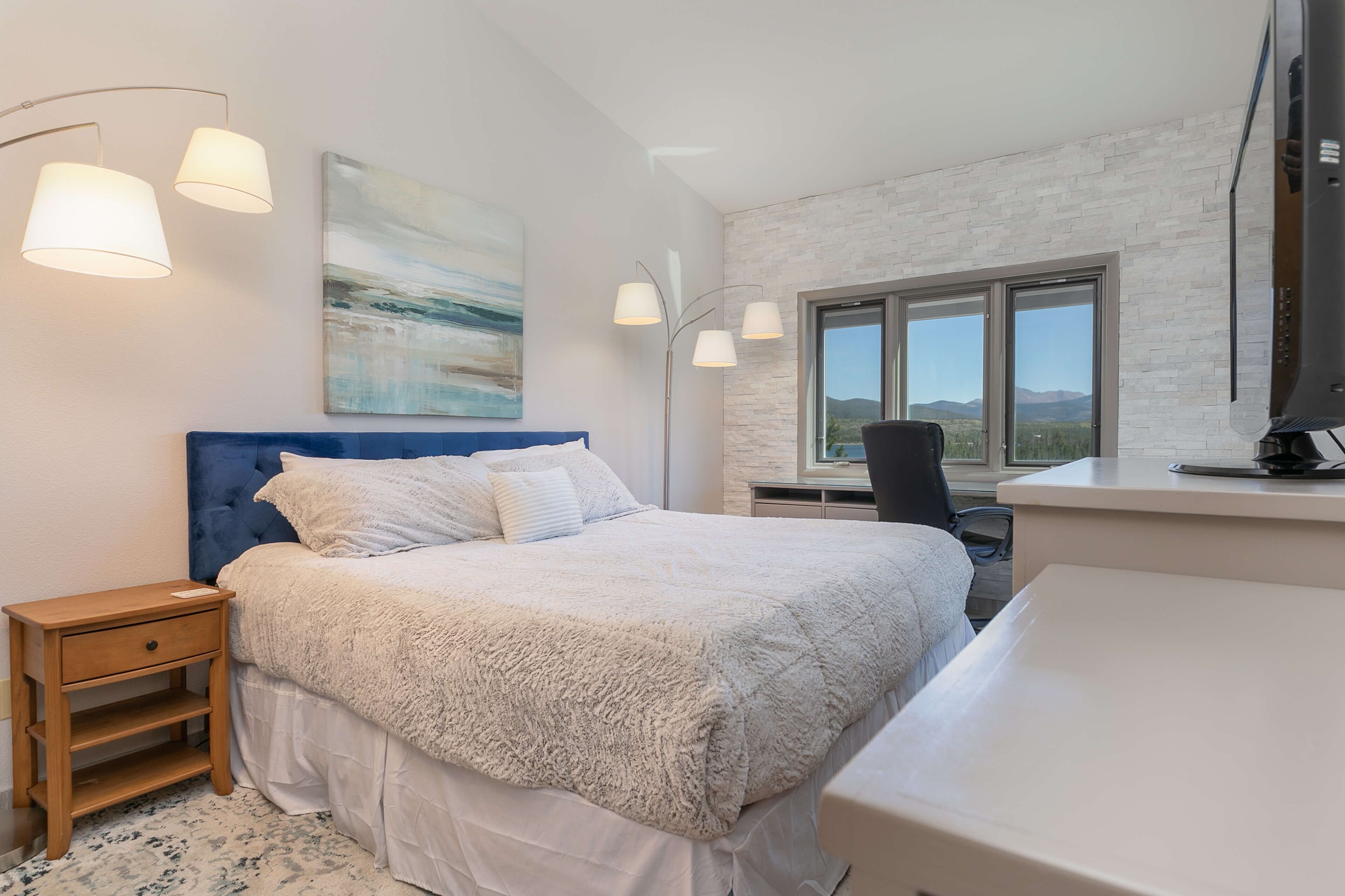 Een slaapkamer met een groot bed, een bureau, een stoel en een raam met uitzicht op de bergen.