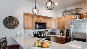 A modern kitchen with wooden cabinets, stainless steel appliances, a marble countertop, and a fruit bowl. - Fourth & Main Condo: Heart of Frisco (Frisco)