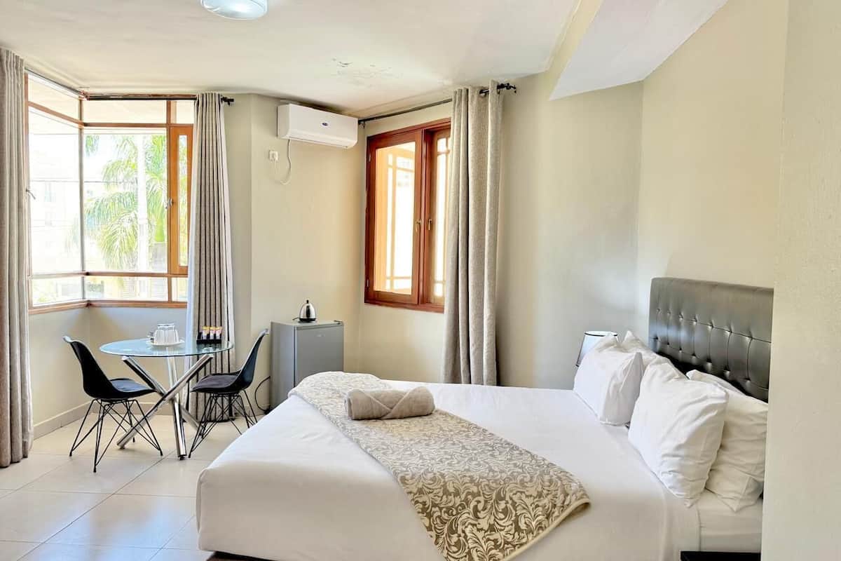 Une chambre d’hôtel avec un grand lit, un bureau avec des chaises, une fenêtre avec des rideaux et un appareil de climatisation.
