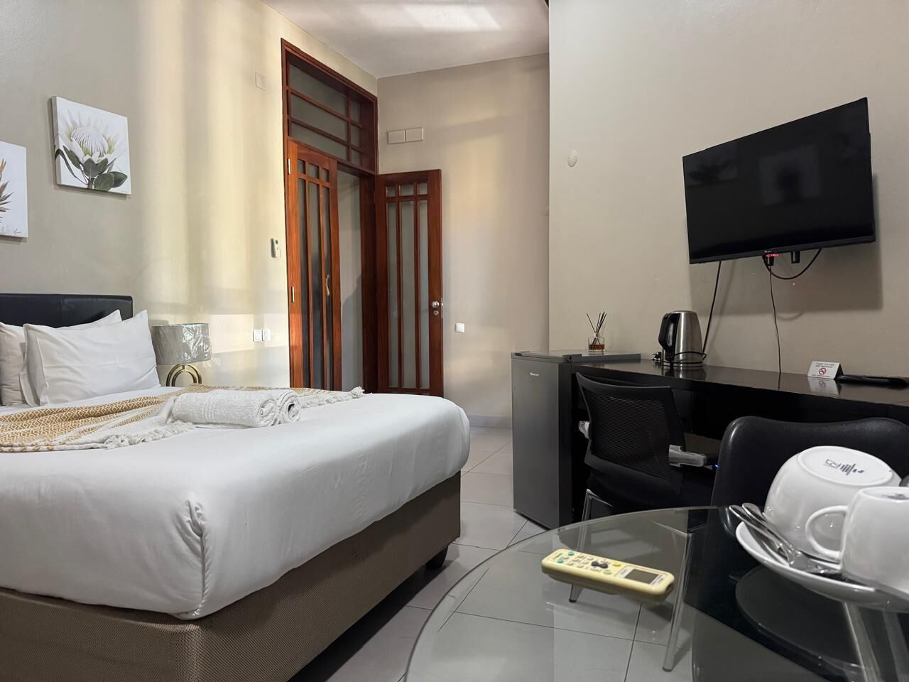 A hotel room with a bed, a desk, a television, a coffee maker, and a remote control.