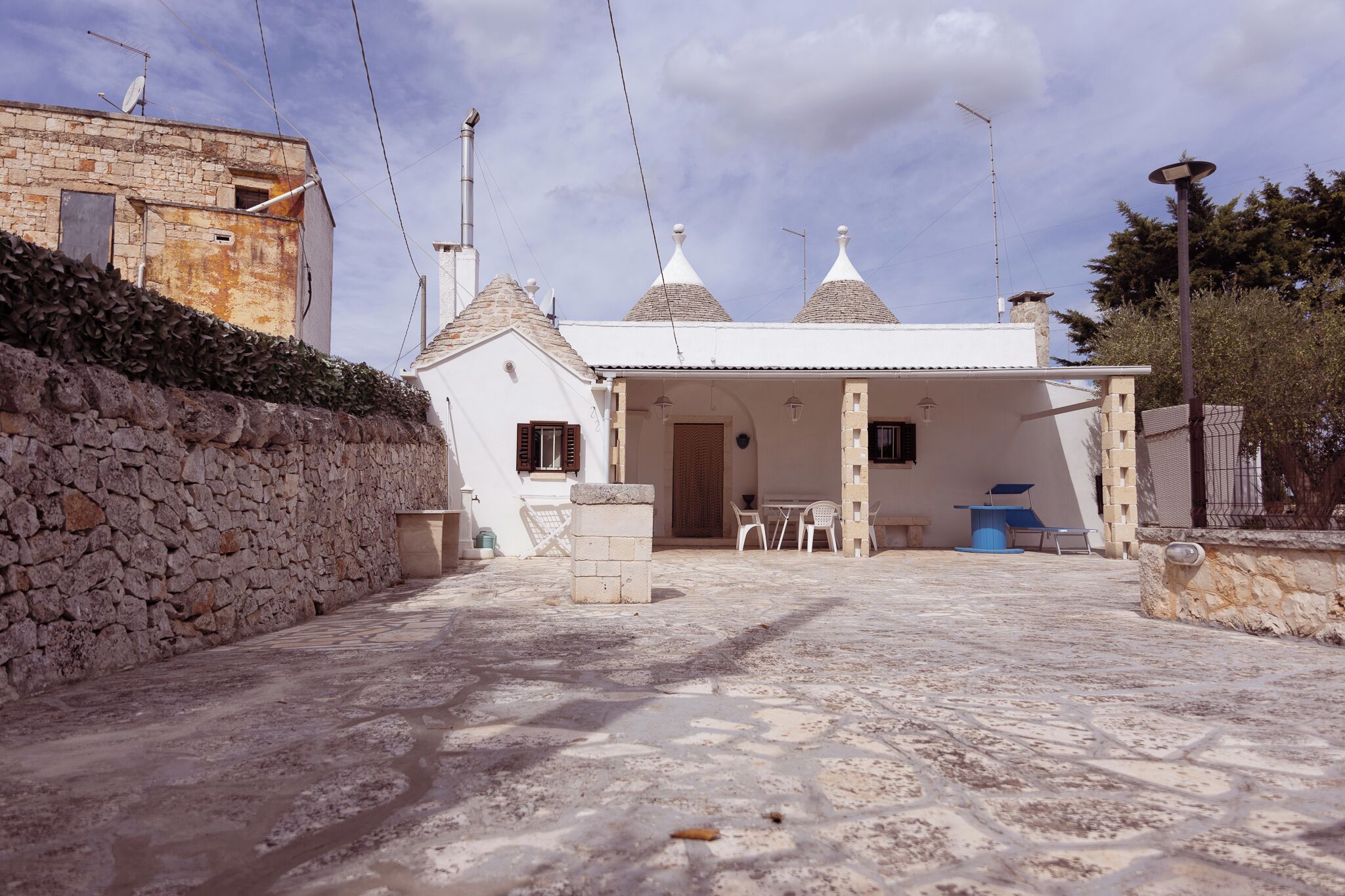 Un patio de piedra con un edificio blanco, tejado de baldosas y un pequeño espacio exterior con mobiliario.