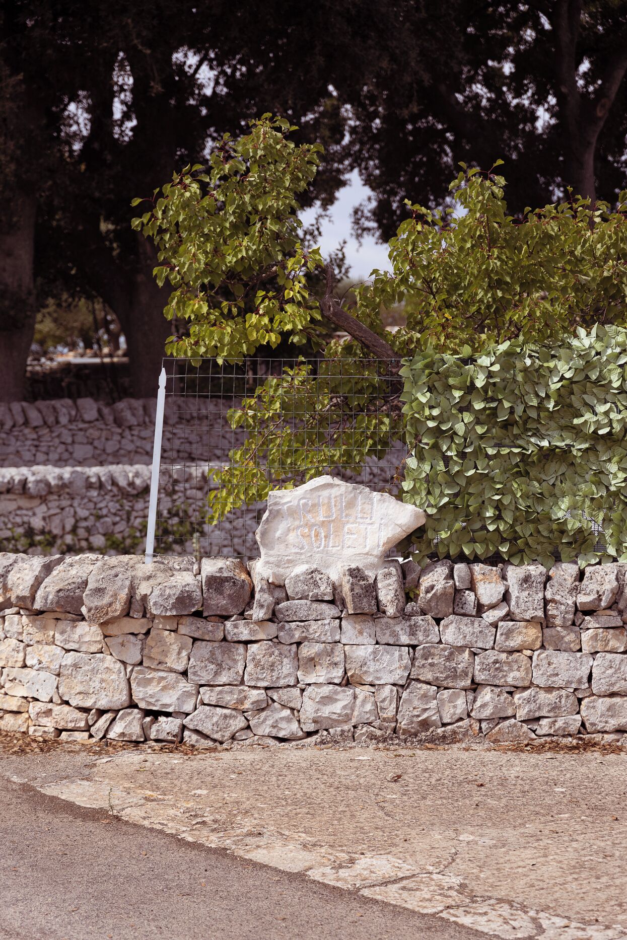 Eine Steinmauer mit einem Metallzaun und einem Schild, auf dem 'TRULY SOLELY' steht.