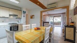 Een moderne keuken met witte kasten, een gele geruit tafel en een eethoek met witte stoelen.