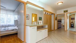 Een moderne, goed verlichte kamer met een bed, een bureau met glazen blad en een keukenhoek zichtbaar door een open deur.