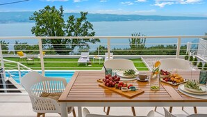 A terrace with a wooden table set for breakfast, overlooking a pool and a scenic view of a lake and mountains. - 2-bedroom Villa La Vita with private heated 33sqm pool (Jesenice)