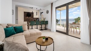 A modern living room with a sofa, a coffee table, and a view of a balcony with outdoor seating. - 2-bedroom Villa La Vita with private heated 33sqm pool (Jesenice)
