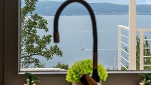 A window with a view of a body of water and distant land, a faucet, and two potted plants on a windowsill. - 2-bedroom Villa La Vita with private heated 33sqm pool (Jesenice)