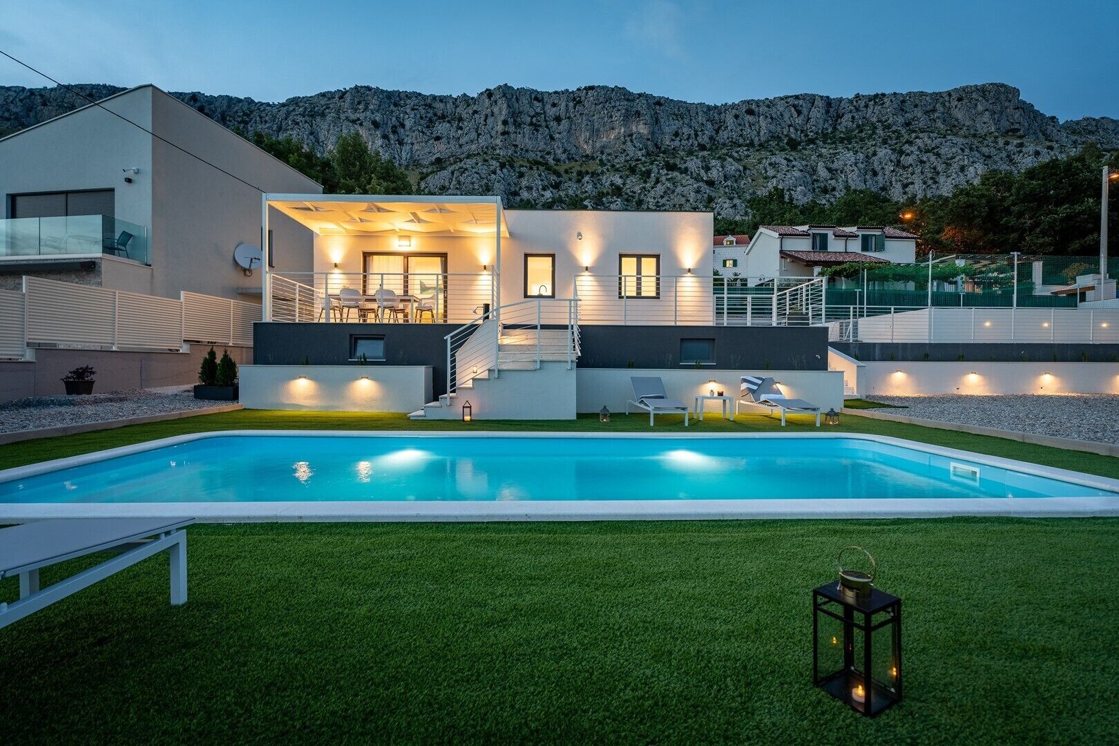 Una casa moderna con piscina, mobiliario exterior y un telón de fondo montañoso.
