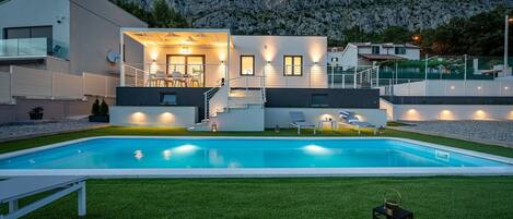 Una casa moderna con piscina, mobiliario exterior y un telón de fondo montañoso.