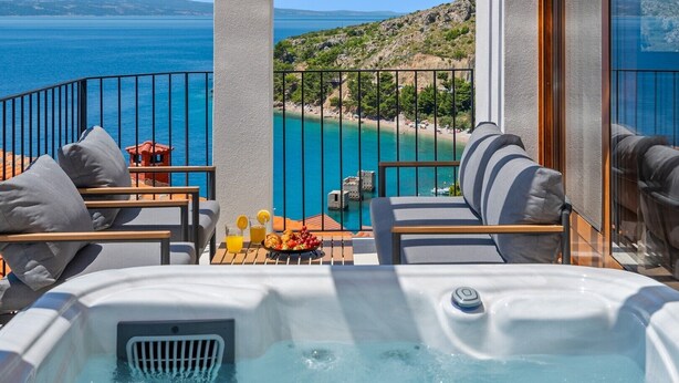 Un balcón con bañera de hidromasaje, mobiliario exterior y vista al mar y la playa.