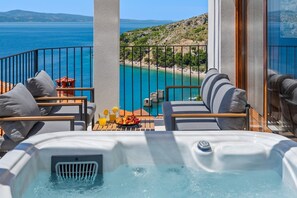 Un balcon avec un jacuzzi, un espace salon extérieur et une vue sur la mer et la plage.