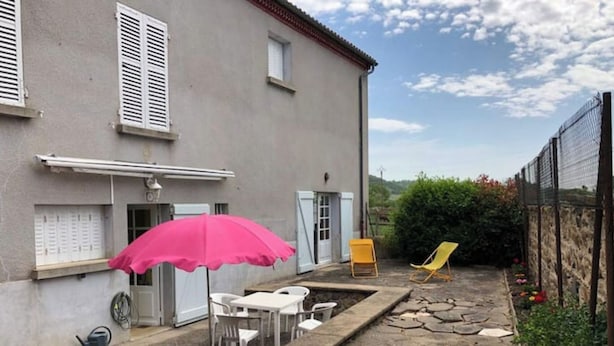 Een binnentuin met een pad van stenen, een roze parasol, witte stoelen en een gele stoel.