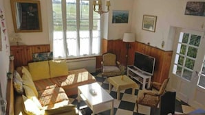 Een woonkamer met een bank, fauteuils, een salontafel, een televisie en een raam met gordijnen.