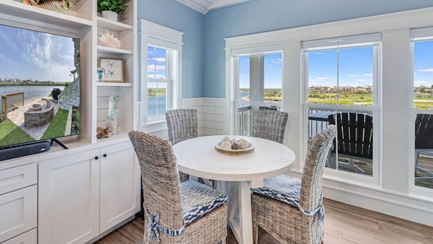 A coastal home interior with a round dining table, wicker chairs, and a view of the ocean. - Nauti Capitan: Where the ocean’s call is always heard, and adventure awaits. (Port Aransas)