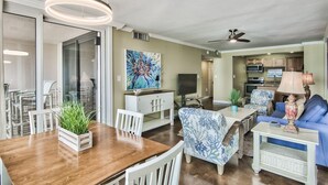 Amplia sala de estar con mesa de comedor, sillas, un sofá, televisión y cocina al fondo.