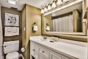 A bathroom with a white sink, a large mirror, and a toilet. There are towels hanging on hooks and a framed picture on the wall. - Sunset Jetty View! Enjoy one free beach chair set up and umbrella each day! (Destin)