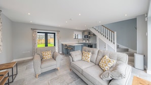 A modern living room with a grey sofa set, a wooden coffee table, and a view of a kitchen and outdoor area. - No 1 The Coach House (Carnforth)