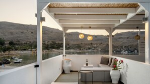 A balcony with a view of a body of water, a white wall, a seating area, and hanging lights.