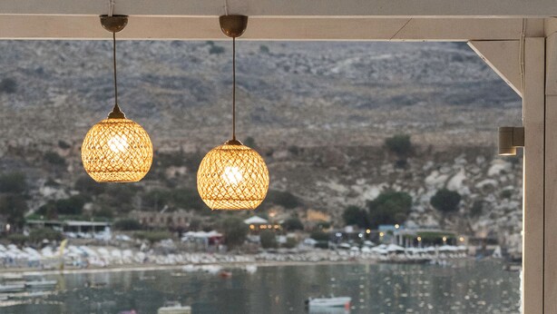 A balcony with a seating area, a table with a bottle and glass, and a view of boats on water.