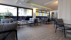 Un espace de détente intérieur moderne, avec des chaises et des tables à revêtement gris, de grandes fenêtres et un plancher en bois.