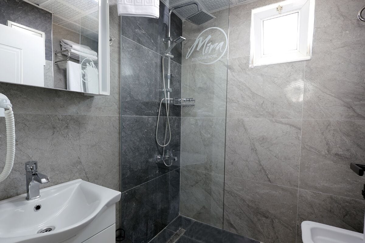 Un baño moderno con ducha envuelta en vidrio, lavamanos blanco y espejo de tocador.