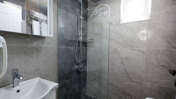 Un baño moderno con ducha envuelta en vidrio, lavamanos blanco y espejo de tocador.